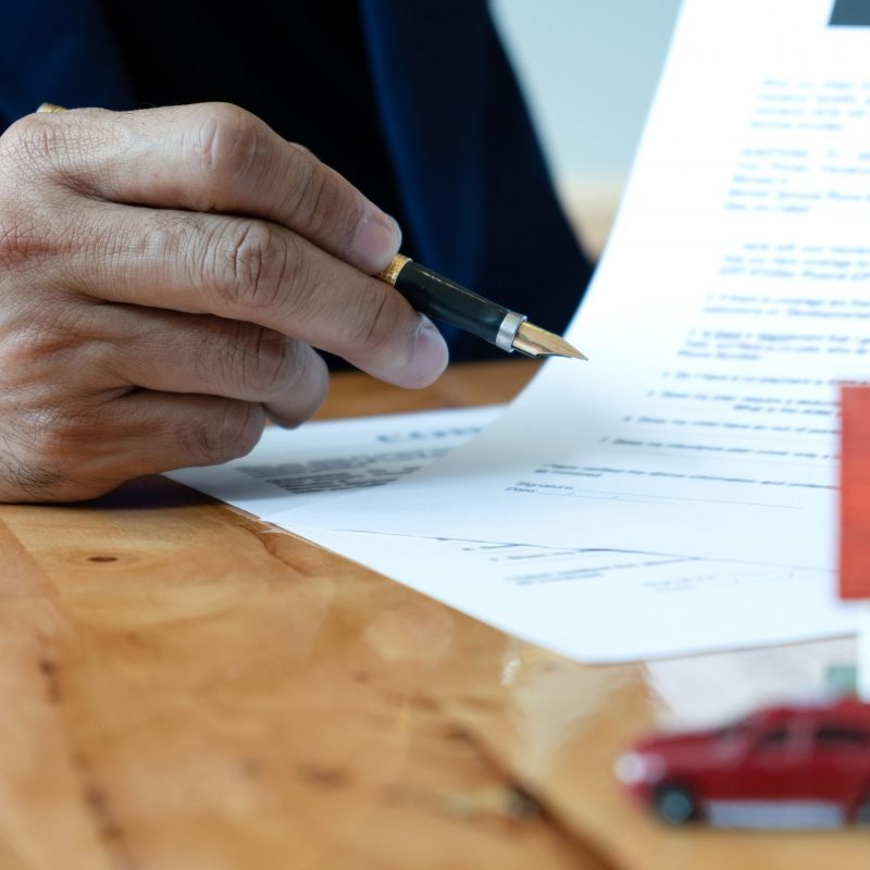 Broker house hold pen pointing at document.Model house, model car on the table